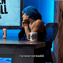 a woman with blue hair is sitting at a desk with a mug that says broken skull on it
