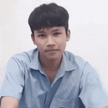 a young man in a blue shirt is making a funny face and looking at the camera .