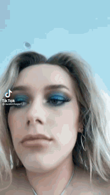 a close up of a woman 's face with blue eyeshadow and earrings .