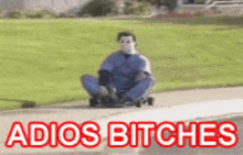 a man wearing a mask is sitting on a skateboard with the words adios bitches below him .