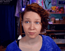 a woman in a blue shirt is looking at the camera with a sign behind her that says " redt resub x37 "