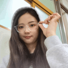a girl wearing glasses and a hoodie is holding a pair of clear glasses