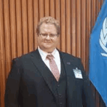 a man in a suit and tie is standing next to a flag .