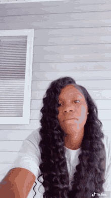 a woman with long curly hair is standing in front of a window and taking a selfie .