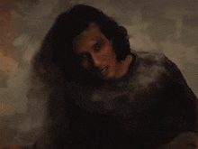 a man with long hair leaning against a white wall