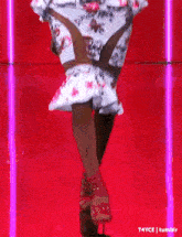 a woman is walking down a red runway wearing a floral dress and red shoes .