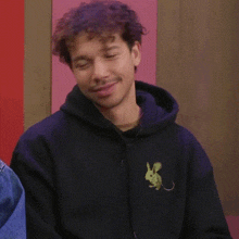 a man with curly hair is wearing a black hoodie with a dragon on it