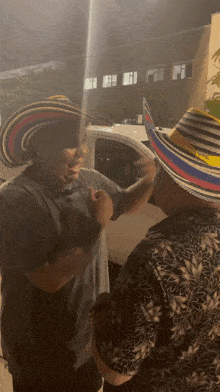 two men wearing colorful hats are standing in front of a car