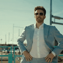 a man wearing sunglasses and a light blue suit is standing with his hands on his hips