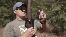 a man is holding a rifle in his hands while wearing a just shirt .