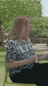 a woman in a black and white shirt is sitting in a chair in the park .