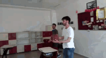 a man is throwing a basketball in a classroom while another man watches .