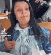 a woman in a denim jacket and a white hoodie is making a funny face .