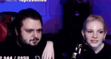 a man and a woman are sitting next to each other in front of a microphone in a dark room .