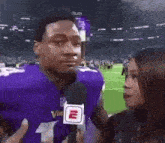 a man in a purple vikings jersey is being interviewed by a woman in front of a microphone .