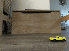 a yellow toy car is sitting on a wooden floor next to a wooden box
