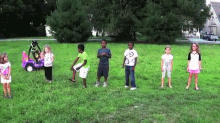 a group of children are standing in a grassy field with a purple car in the background
