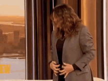 a woman in a suit is standing in front of a window with the letter w on the bottom right