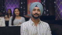 a man wearing a turban and striped shirt smiles for the camera