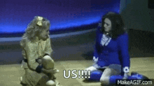 two women are kneeling on the floor on a stage and talking to each other .