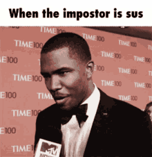 a man in a suit and bow tie is talking into a mtv microphone in front of a wall that says time 100