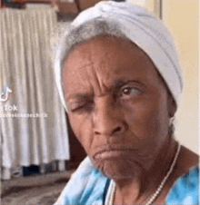 an elderly woman wearing a white headband and pearls is making a funny face .