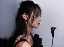 a woman with long black hair is holding a black flower in her hand