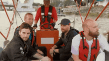 a group of men sitting on a boat with one wearing a life jacket