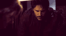 a man with a beard is wearing a leather jacket and looking down at something .
