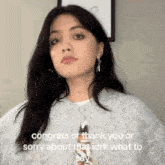 a woman is wearing a grey sweater and earrings and says congrats or thank you or sorry about that idk what to say