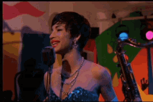 a woman in a blue dress is singing into a microphone while holding a saxophone