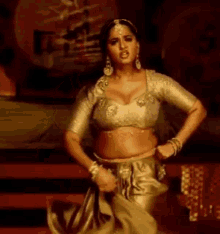 a woman in a crop top and a gold skirt is dancing on a stage .
