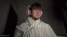 a man is wrapped in a blanket and wearing pink headphones .