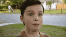 a young boy is making a funny face while a man is mowing the grass .