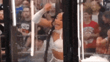 a woman in a white bra is dancing in front of a crowd in a cage .