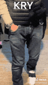 a man wearing a black vest and jeans has the word kry written on his pants