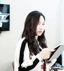 a girl with long hair is holding a tablet in front of a tv screen that says tk .