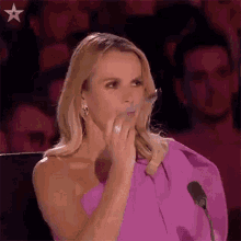 a woman in a pink dress is sitting in front of a microphone and covering her mouth .