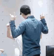 a man wearing a hat and a denim shirt is dancing in front of a wall .