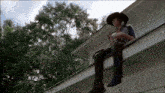 a man in a cowboy hat is sitting on the roof of a house