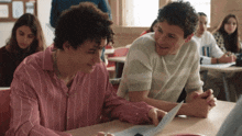 two young men sit at a desk in a classroom