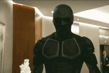 a man in a black suit is standing in a hallway looking at the camera