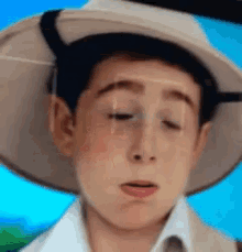a boy wearing a hat and a white shirt is making a sad face