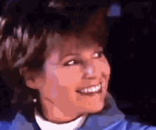 a woman in a blue jacket and white sweater smiles
