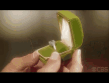 a person is holding a green box with an engagement ring in it