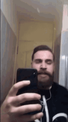 a man with a beard and mustache is taking a selfie with his phone