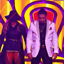 a man in a white suit is standing next to a woman in a hat