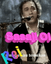 a man singing into a microphone while holding a guitar with the words sasaj oi written in pink