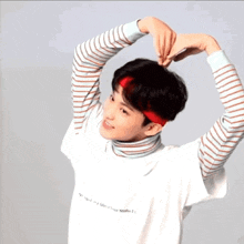 a young man wearing a striped shirt and a red headband making a heart shape with his hands