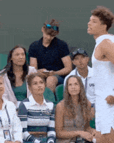 a man in a white tank top is standing in front of a group of people sitting in a stadium .